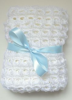 two white crocheted blankets with a blue ribbon on the top one is folded