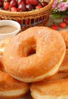 doughnuts are piled on top of each other near a basket of cherries