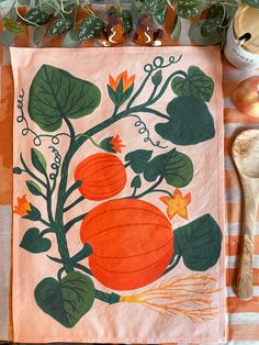 a kitchen towel with an orange pumpkin and green leaves on it next to a wooden spoon