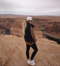 a woman standing on the edge of a cliff looking out at canyons and cliffs