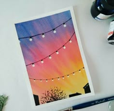 a card with string lights on it sitting next to some watercolor pens and markers