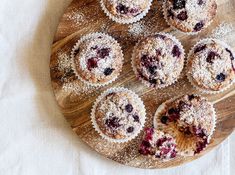 several blueberry muffins on a wooden plate with powdered sugar