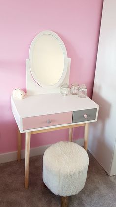 a white vanity with a mirror and stool in a pink walled room next to a door