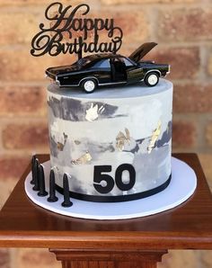 a birthday cake with a car on top and the number fifty written in gold foil