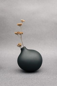 a black vase with flowers in it on a gray surface and the bottom half is empty