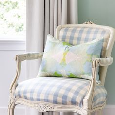 a blue and white checkered chair with a pillow on it's back in front of a window