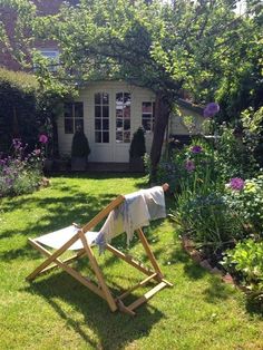 a lawn chair sitting in the middle of a yard next to flowers and bushes with a towel draped over it