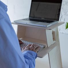 a person sitting at a desk using a laptop on top of a wooden stand with a plant in front of them