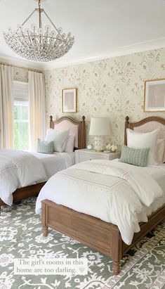 two twin beds in a bedroom with floral wallpaper and chandelier above them