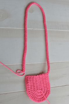 a pink crocheted purse sitting on top of a white wooden floor next to a string