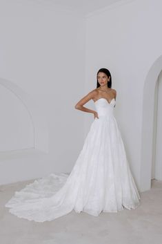 a woman in a white wedding dress standing next to a wall and posing for the camera