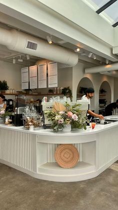 a man is behind the counter at a restaurant with flowers in front of him and other people standing around