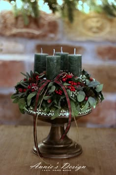 two candles are sitting on top of a christmas centerpiece with holly and red berries