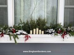 a window sill decorated with evergreens, pine cones and candles in the snow