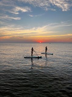 two people stand up paddle boarding in the ocean at sunset or dawn with one person standing on board