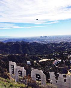 an airplane flying over the hollywood sign on top of a hill with mountains in the background