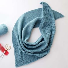 a blue scarf, scissors and yarn on a white table with some knitting needles in front of it