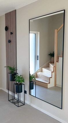 a mirror sitting on the side of a wall next to potted plants and a stair case