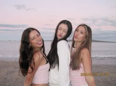 three young women standing next to each other near the ocean