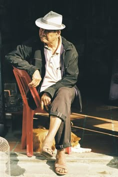 an old man sitting on a bench next to a dog and wearing a white hat