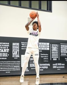 a young man holding a basketball on top of a gym floor in front of a wall