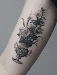 a woman's arm with flowers in a vase tattoo on the left inner arm