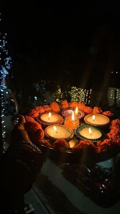 a person holding a tray with lit candles in the middle of it at night time