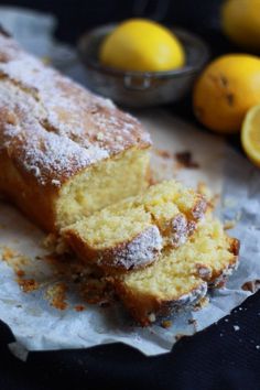 a loaf of lemon bread sitting on top of a piece of paper next to some lemons