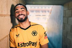 a man in a yellow shirt is smiling and looking up at the camera while standing next to a brick wall