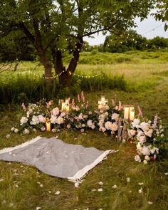 an outdoor ceremony with candles, flowers and blankets on the ground in front of a tree