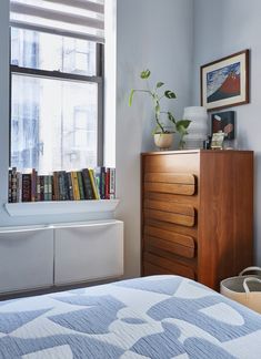 a bedroom with a bed, dresser and bookshelf next to a large window