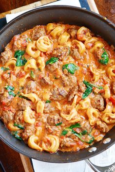 a skillet filled with pasta and meat covered in sauce on top of a wooden table