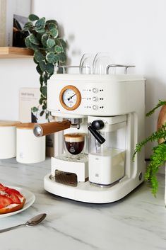 a white coffee maker sitting on top of a counter next to a plate of food