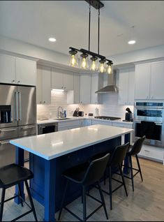 an island in the middle of a kitchen with stools and lights hanging from it