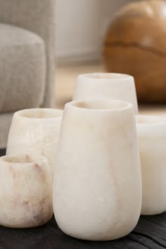 three white vases sitting on top of a wooden table next to a gray couch