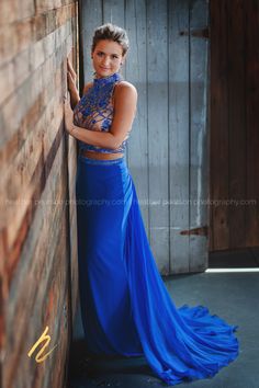 a woman in a blue dress leaning against a wooden wall