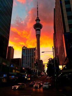 the sky is pink and orange as cars drive down the street in front of tall buildings