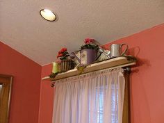 a window sill with coffee cups and watering cans on it, in front of a pink wall