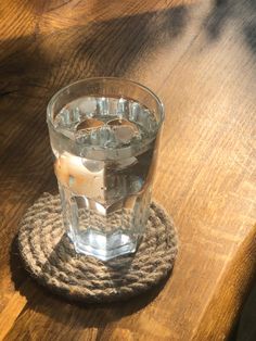 a glass of water sitting on top of a wooden table next to a rope coaster