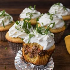 several cupcakes with white frosting and green leaves on top are sitting on tin foil