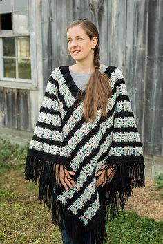 a woman standing in front of a barn wearing a black and white striped ponchle