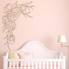 a white crib with a pink wall and floral decal on the wall behind it