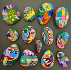 painted rocks are arranged in the shape of fish and other colorful shapes on a gray surface