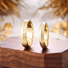 two gold wedding rings sitting on top of a wooden stand