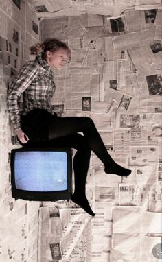 a woman sitting on top of a tv in front of a wall covered with newspapers