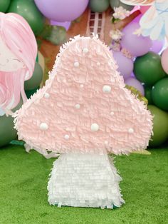 a cake shaped like a mushroom sitting on top of a green grass covered field with balloons in the background