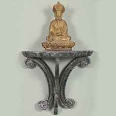 a golden buddha statue sitting on top of a metal shelf next to a white wall