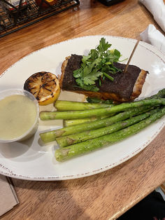 a white plate topped with asparagus and meat next to a bowl of sauce