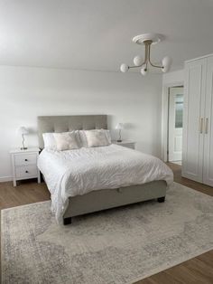 a large white bed sitting in a bedroom on top of a hard wood flooring