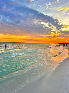 people walking on the beach at sunset with colorful clouds in the sky over the water